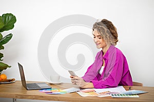 Smiling Young Female Designer Using Smartphone At Workplace In Home Office