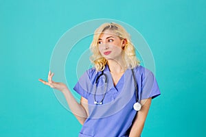 Smiling young female doctor or nurse wearing blue scrubs and stethoscope, pointing and looking to side