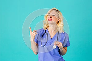 Smiling young female doctor or nurse wearing blue scrubs and stethoscope, pointing and looking to side