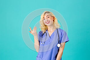 Smiling young female doctor or nurse wearing blue scrubs and stethoscope, pointing up