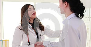 Smiling young female doctor shaking hands after concluding health insurance contract with male patient