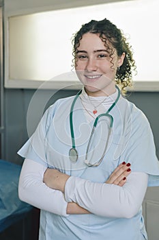 Smiling young female doctor wearing white coat and stethoscope with arms crossed looking at camera