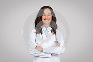 Smiling young female doctor wearing white uniform and stethoscope standing with folded arms and smiling