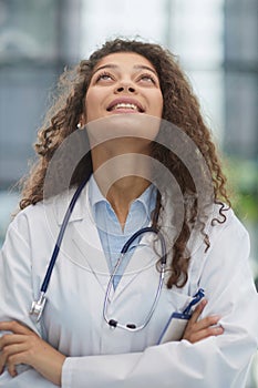 Smiling young female doctor in white coat looking up