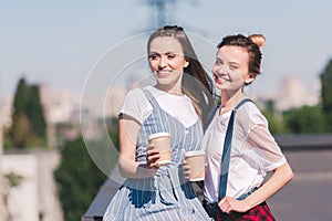 smiling young female friends with paper cups of coffee