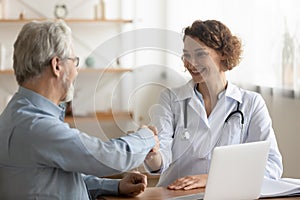 Smiling young female general practitioner shaking hands with old patient.