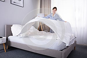 Housekeeper Arranging Bedsheet On Bed