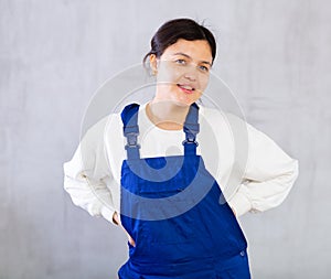 Smiling young female mechanic in blue overalls posing in studio