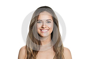 Smiling young female model with healthy hair, makeup and shiny clear skin posing against white studio wall background.