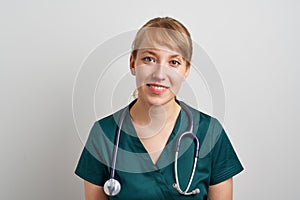 Smiling young female nursing assistant with phonendoscope in green uniform. Surgeon emergency