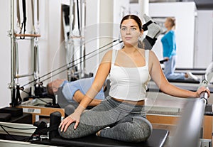 Smiling young female in sportswear training twist rotation while using Pilates performer bed in gym