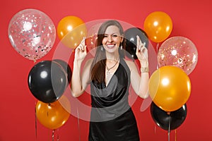 Smiling young girl in black dress celebrating wait for special moment, keeping fingers crossed, making wish on bright