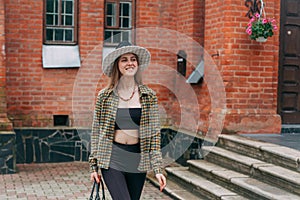 A smiling young girl with blond long hair, in black leggings, a tank top, a beige jacket and a hat