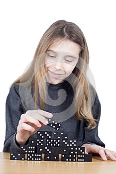 Smiling Young Girl Building A Tower Of Black Dominoes With Patience On Wooden Table Isolated On White Background