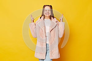 Smiling young girl with funny ponytails standing isolated over yellow background holding fingers crossed for good luck having