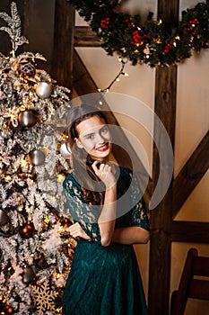 Smiling young girl in green dress with presents and gift boxes under the Christmas tree