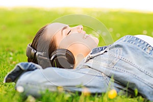 Smiling young girl in headphones lying on grass