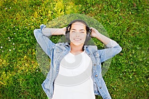 Smiling young girl in headphones lying on grass