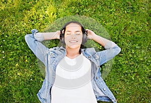 Smiling young girl in headphones lying on grass