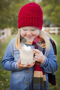 Smiling Young Girl Holding Cocoa Mug with Marsh Mallows Outside