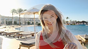 Smiling young girl, looking at camera. Beautiful woman in red swimsuit near the blue swimming pool on hot sunny day