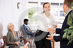 Smiling young girl makes deal, shaking hands with man colleague while standing in office.