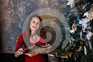 Smiling young girl in red dress with presents and gift boxes under the Christmas tree