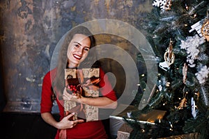 Smiling young girl in red dress with presents and gift boxes under the Christmas tree