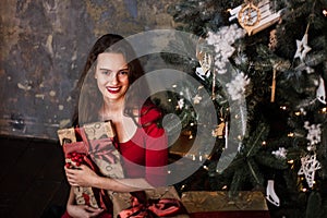 Smiling young girl in red dress with presents and gift boxes under the Christmas tree