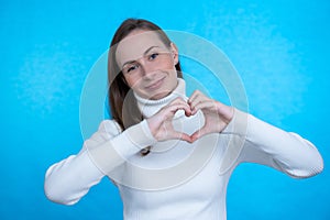 Smiling young girl showing heart with two hands, love sign.  over blue background