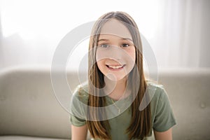 Smiling young girl sit on sofa looking at camera