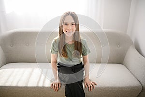 Smiling young girl sit on sofa looking at camera
