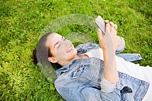 Smiling young girl with smartphone lying on grass