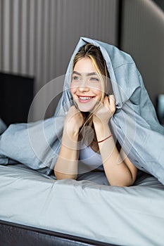 Smiling young girl under a duvet in her bedroom