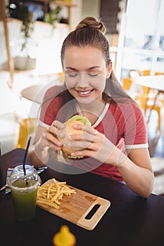 Smiling young gorgeous woman eating burger at coffee shop