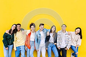 Smiling young group of multiracial happy friends leaning on yellow wall