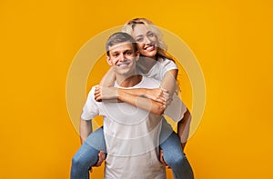 Smiling young guy carrying girlfriend on his back