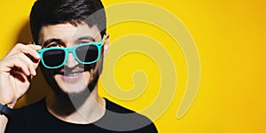 Smiling young guy wearing glasses. Close-up portrait on yellow background with copy space.