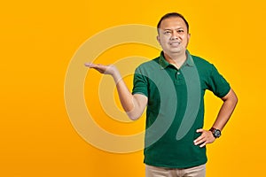 Smiling young handsome man showing copy space on palm on yellow background