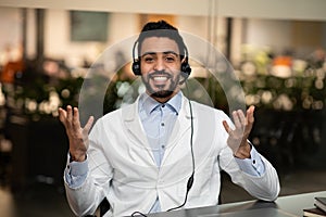 Smiling young handsome middle eastern engineer or doctor in headphones gestures, look at camera