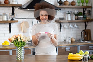 Smiling young happy african american woman at home looking at positive pregnancy test