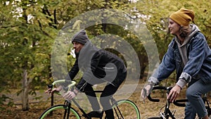 Smiling, young hipster couple enjoying cycling through park on trekking bikes. Two young people in hats having great