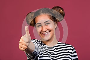 Smiling young hipster girl with playful hairstyle making ok hand gesture isolated over pink background