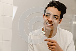 Smiling young hispanic man brushing teeth