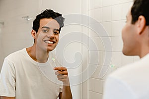 Smiling young hispanic man brushing teeth