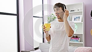 Smiling young hispanic man happily teleworking at home - agent for a call center, hands-free call gadget on, savoring coffee in