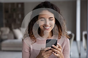 Smiling young hispanic woman reading pleasant message on cellphone.