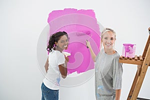 Smiling young housemates painting wall pink