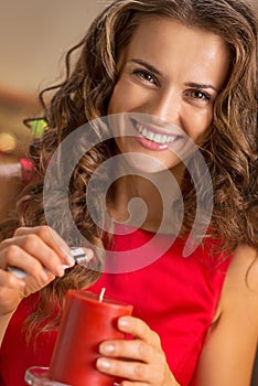 Smiling young housewife lighting candle in christmas decorated k