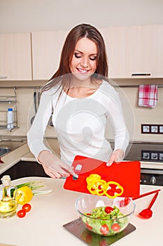 Smiling young housewife mixing fresh salad